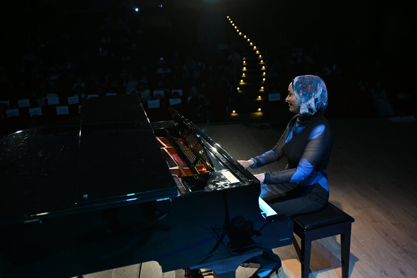 Yasmin Shennawy playing the piano lit from above on a darkened stage